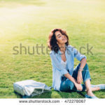 stock-photo-nice-brunette-girl-with-short-hair-is-chilling-on-grass-in-park-she-wears-white-t-shirt-shirt-472278067